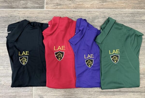 Four different colored shirts with the letters lae on them.