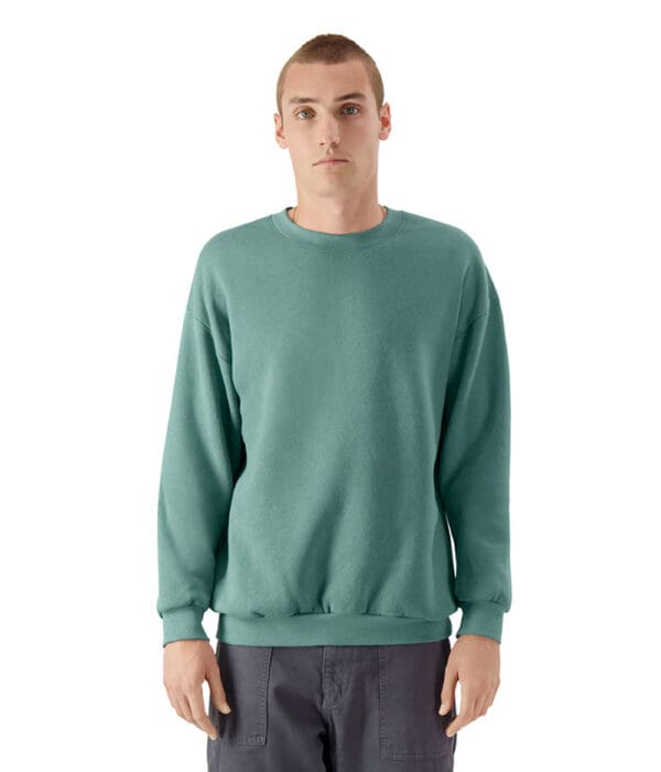 A man wearing a green sweatshirt standing in front of a white wall.