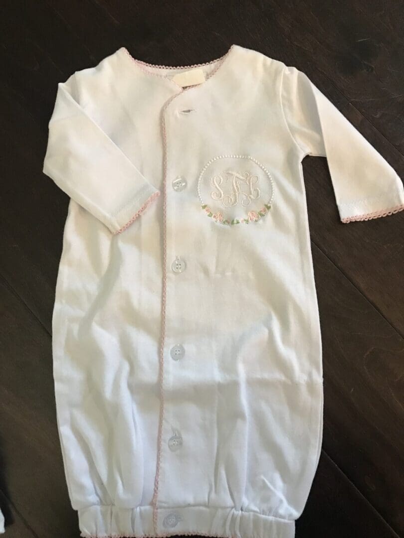 A white baby gown with pink trim on the bottom.