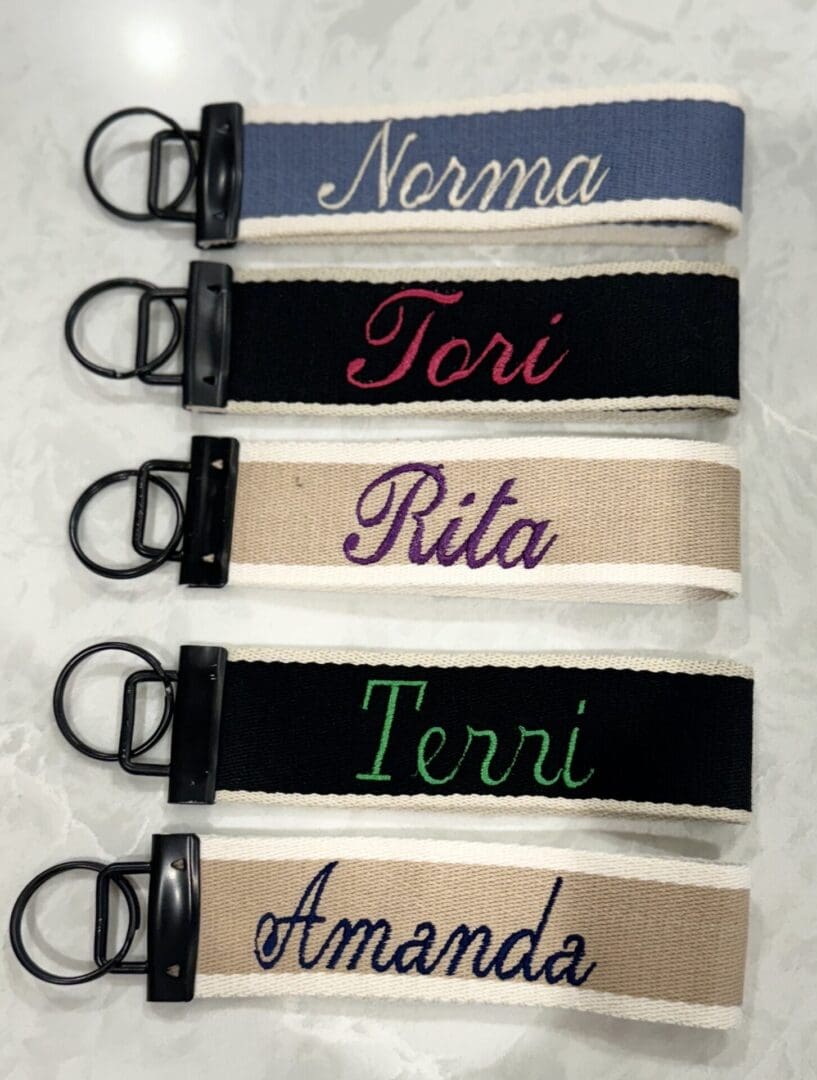 A group of six key chains with the names of five different people.