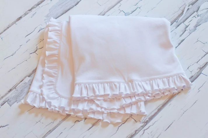 A white blanket with ruffles on top of it.